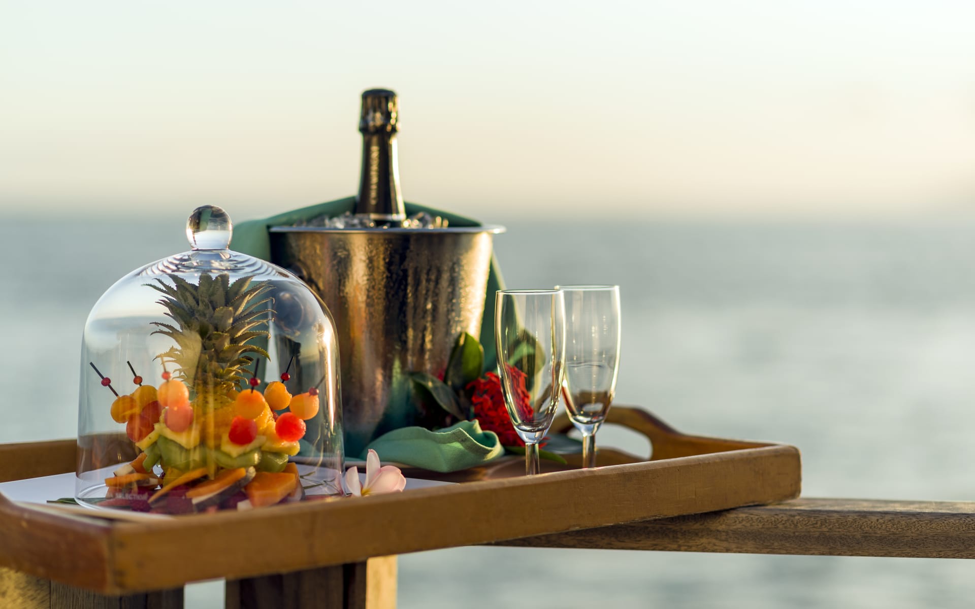 A tray is full of a bucket with champagne, glasses and food. 